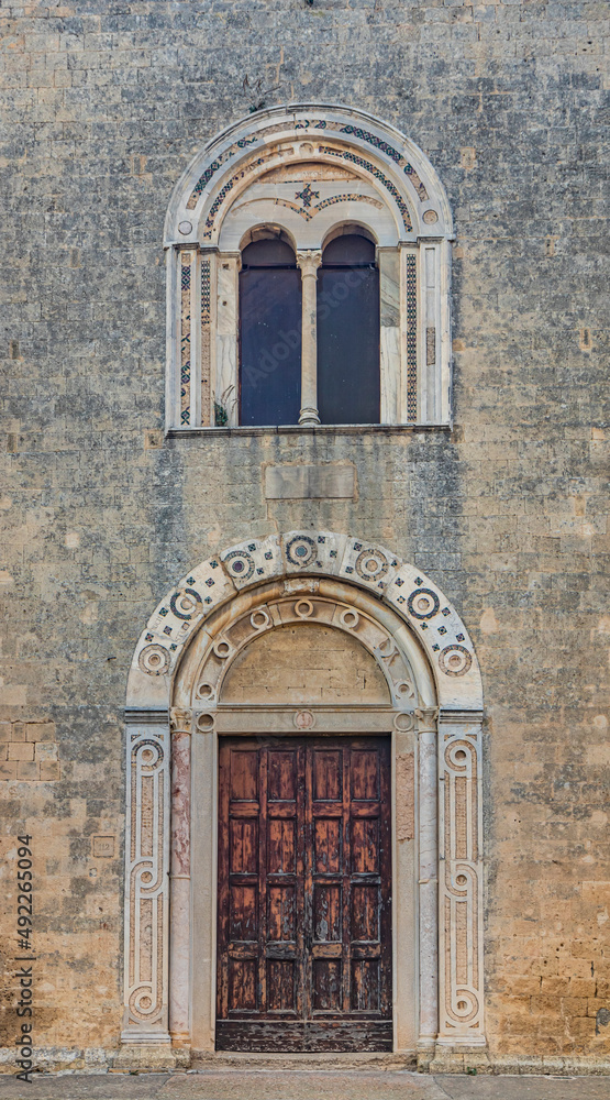 The village of Tarquinia, Viterbo, Lazio, Italy - Facade of the Church of Santa Maria in Castello, in Romanesque style. Detail, closeup of the arched doors and the mullioned window. TStone brick wall.