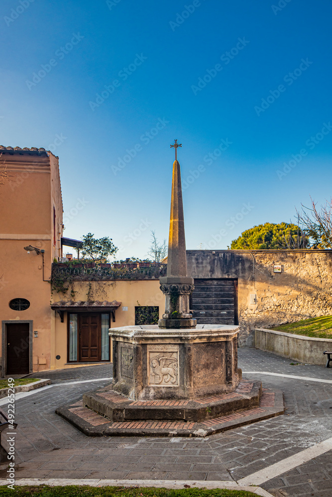 The village of Tarquinia, Viterbo, Lazio, Italy - An ancient octagonal fountain with obelisk and cross. The blue sky in the sunset light in the evening.