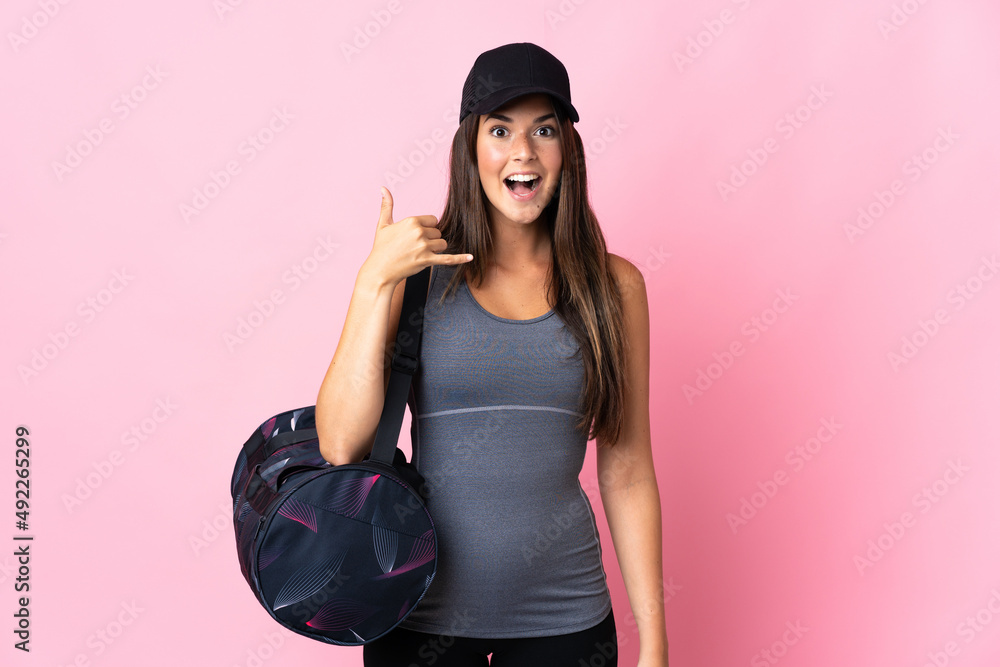Young sport brazilian girl with sport bag isolated on pink background making phone gesture. Call me back sign Young sport brazilian girl with sport bag isolated on pink background making phone gesture. Call me back sign