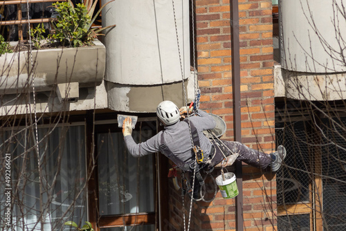 trabajador en altura realizando un trabajo vertical de mantenimiento de fachada estando colgado de cuerdas y llevando un casco y un arnés de seguridad