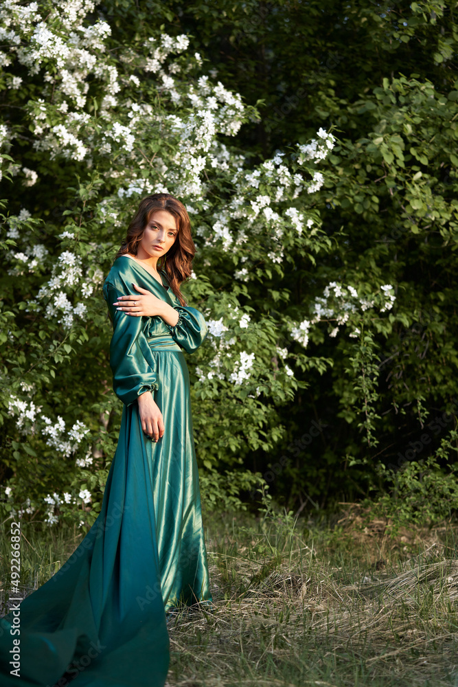A model in a green silk floor-length dress in a blooming apple orchard. Spring. A model in a green silk floor-length dress in a blooming apple orchard. Spring.