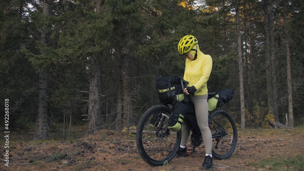 Fototapeta premium The woman travel on mixed terrain cycle touring with bike bikepacking outdoor. The traveler journey with bicycle bags. Stylish bikepacking, bike, sportswear in green black colors. Magic forest park.