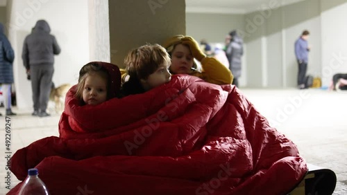 group of little kids, siblings sitting quietly on wooden pallet on the floor in bomb proof shelter during air-raid attack. Sharing one blanket during freezing night. russian invasion to Ukraine