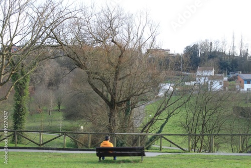 Man in yellow jacket sitting on a bench in nature.