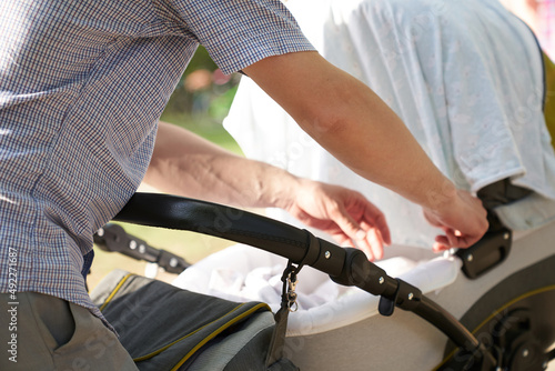 Close-up of men's hands with a stroller. A young father, straightens the cape on the stroller. Father's Day Concept. High quality photo