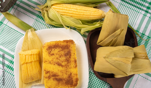 Brazilian Cural, candy corn and pamonha, corn on the cob arranged on a table with a green and white tablecloth, dark background, Top view. photo