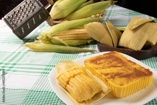 Brazilian Cural, candy corn and pamonha, corn on the cob arranged on a table with a green and white tablecloth, dark background, selective focus. photo