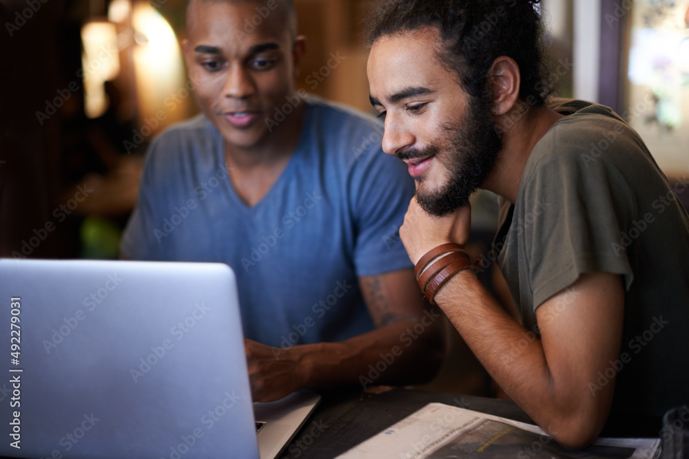 Making the most from the free wifi. Cropped shot of two male friends using a laptop in a coffee shop. Making the most from the free wifi. Cropped shot of two male friends using a laptop in a coffee shop.
