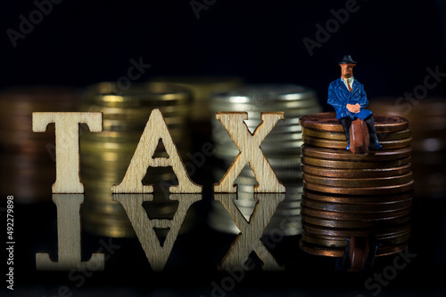 Miniature People. Tax concept.Word Tax and taxman sitting on stacked coins.. Macro photo