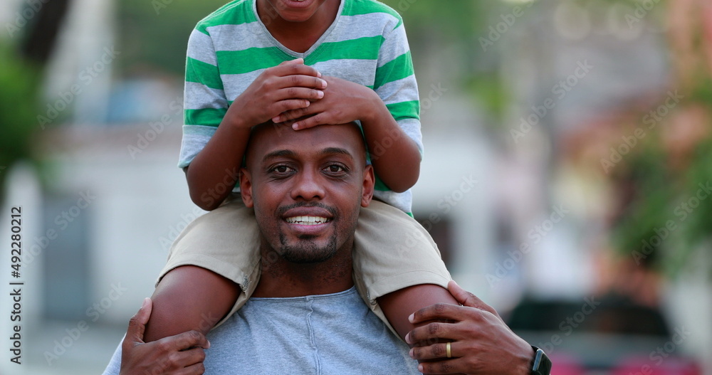 Son on father shoulders. Happy African child and dad bonding together outdoors