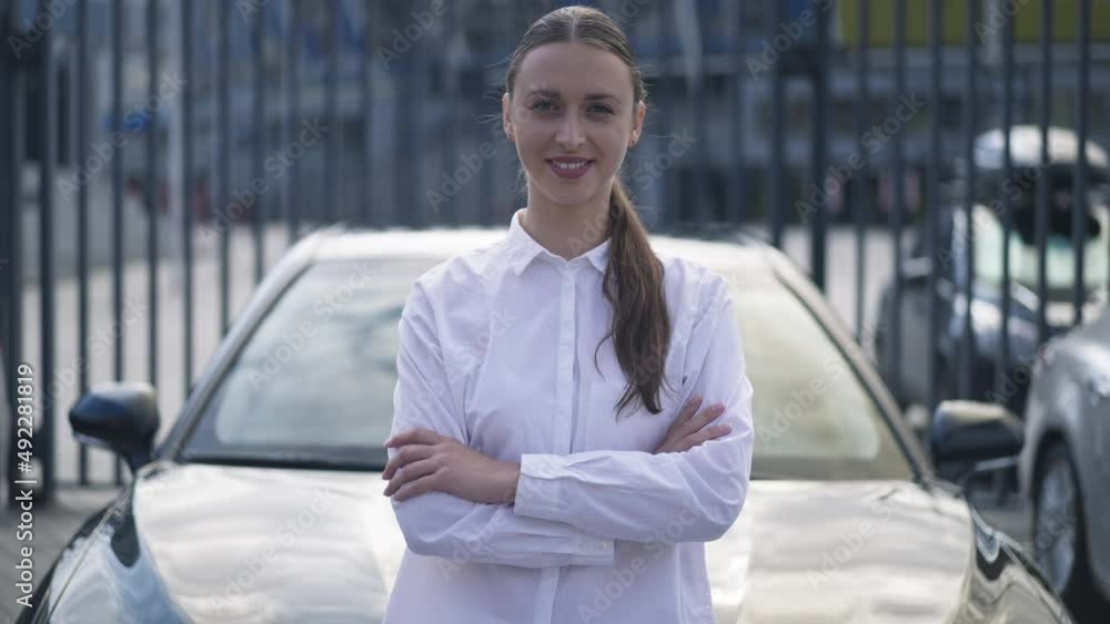 Portrait of satisfied wealthy rich woman crossing hands looking at camera standing at black new car in urban city. Caucasian successful happy businesswoman posing in slow motion outdoors Portrait of satisfied wealthy rich woman crossing hands looking at camera standing at black new car in urban city. Caucasian successful happy businesswoman posing in slow motion outdoors