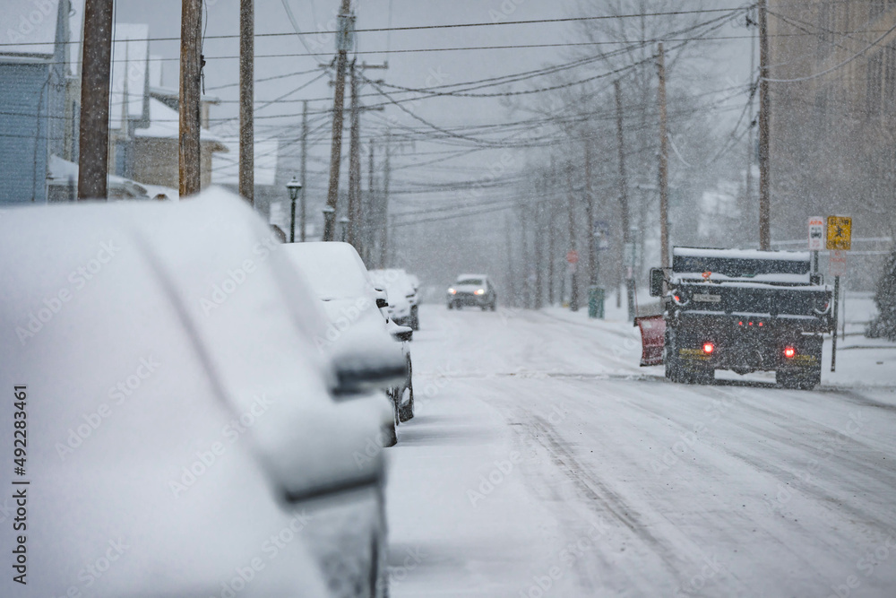 Fototapeta premium Snow storm plow, small USA town road covered in snow, during snow storm, cars traffic, bad weather travel.