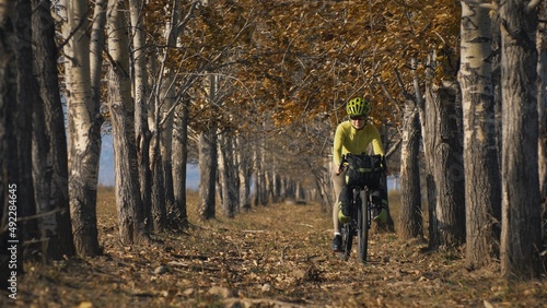 The woman travel on mixed terrain cycle touring with bikepacking. The traveler journey with bicycle bags. Sportswear in green black colors. The trip in magical autumn forest  arch  alley  avenue.