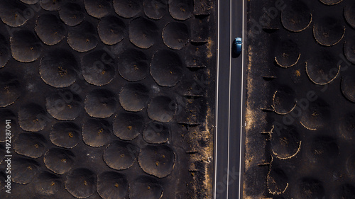 Blue car traveling and driving on a long straight road inscenic volcanic place. Above drone aerial view of people and travel concept. Black sand volcanic ground viewed from vertical view photo