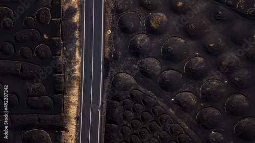 Bycicle rider training and enjoying on a long straight road inscenic volcanic place. Above drone aerial view of people and travel concept. Black sand volcanic ground viewed from vertical view photo