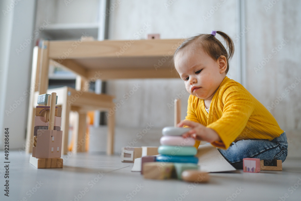 One baby small caucasian infant girl playing on the floor at home copy space holding wooden toys in day front view One baby small caucasian infant girl playing on the floor at home copy space holding wooden toys in day front view