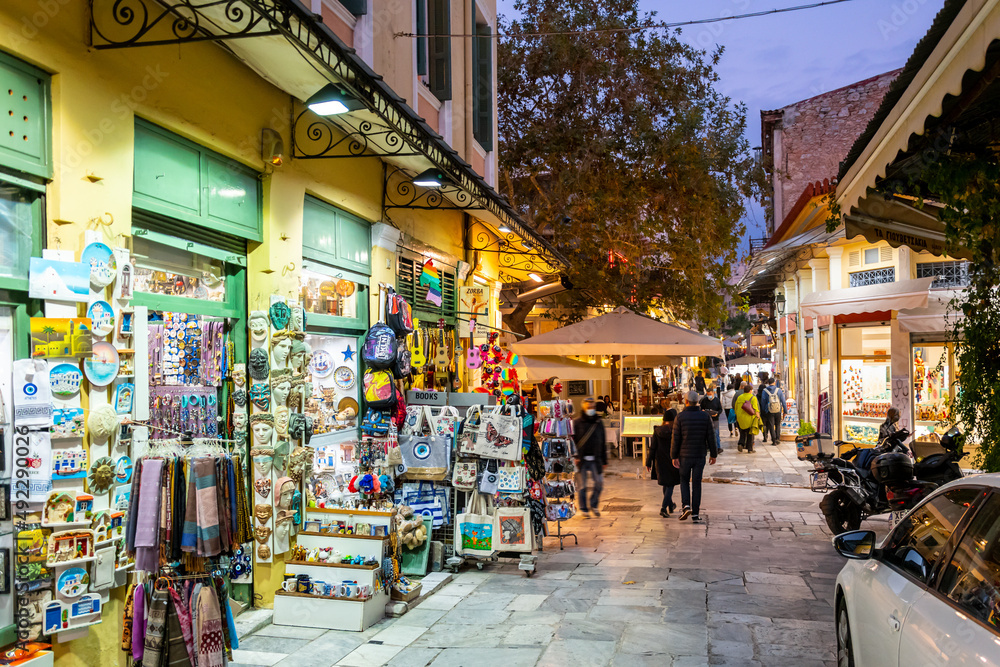 Fototapeta premium A narrow street of gift and souvenir shops and cafes in the colorful illuminated Plaka district at night in Athens, Greece.