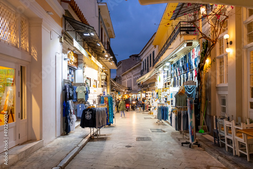 A narrow street of gift and souvenir shops and cafes in the colorful illuminated Plaka district at night in Athens, Greece.