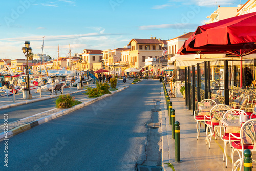 The main street running through the picturesque village of Aegina, on the island of Aegina Greece, with shops and cafes on one side and the marina and port across. photo