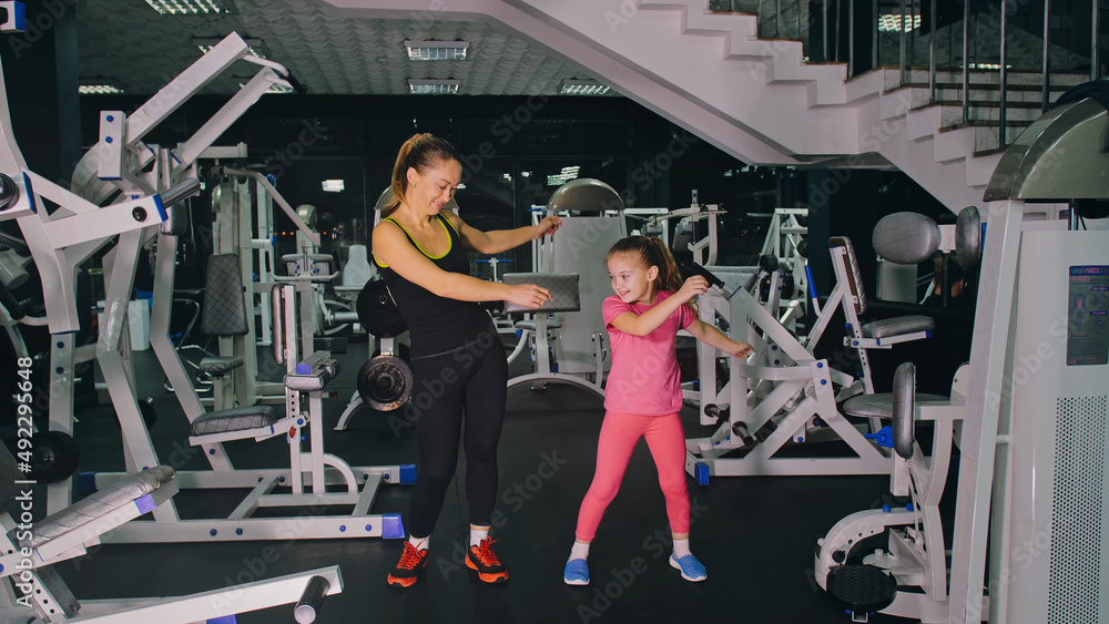 Mother and Daughter in the Gym, Family Performs Physical doing Exercises Fitness, Healthy Lifestyle. Happy Sports Family Training Concept. Woman with her Child doing Stretching Warm-up in the Gym Mother and Daughter in the Gym, Family Performs Physical doing Exercises Fitness, Healthy Lifestyle. Happy Sports Family Training Concept. Woman with her Child doing Stretching Warm-up in the Gym