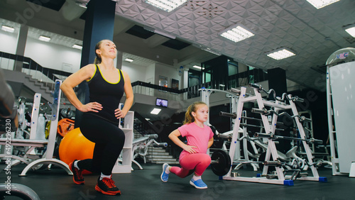 Mother and daughter in the gym, family performs physical doing exercises fitness, healthy lifestyle. Happy sports family training concept. Woman with her child doing stretching warm-up in the gym