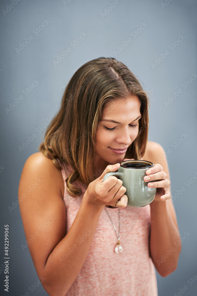 Fresh coffee smells amazing.... Studio shot of a young woman drinking a cup of coffee against a gray background. Fresh coffee smells amazing.... Studio shot of a young woman drinking a cup of coffee against a gray background.