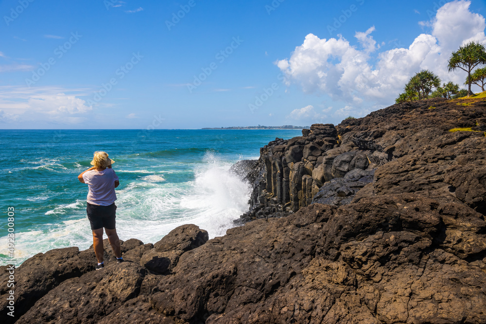 Woman watching a wave breaking against a sea cliff Woman watching a wave breaking against a sea cliff