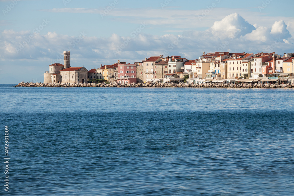 Panorama of  Piran, Slovenia, with the Adriatic sea in front, with blue water and sky, on wharf quay, during a sunny summer afternoon. Piran, or Pirano, is slovenian city on the adriatic sea in istria