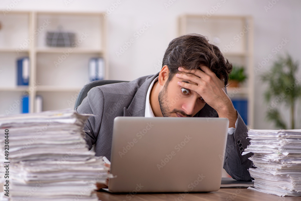 Young male employee unhappy with excessive work in the office Young male employee unhappy with excessive work in the office