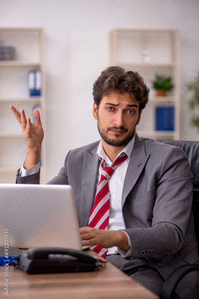Young male employee unhappy with excessive work in the office Young male employee unhappy with excessive work in the office