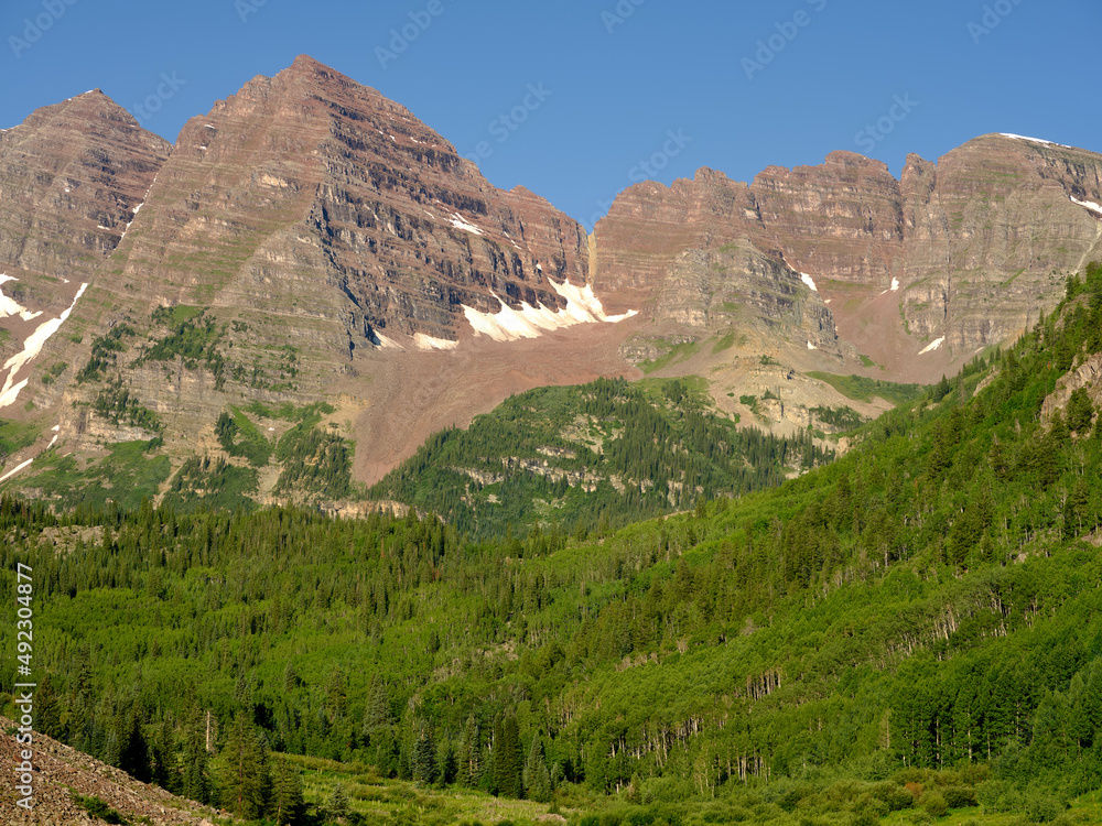 Horizontal image of the red sandstone Maroon Bells with the thick pine forests at the base of the mountains in Colorado