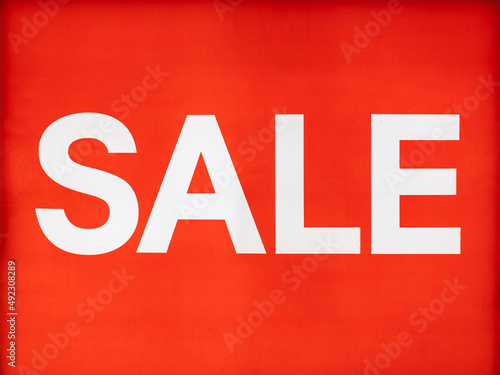 big white sale word or text on light sign in shop behind glass window or wall and red background at shopping mall or department store for advertising on signboard and business marketing