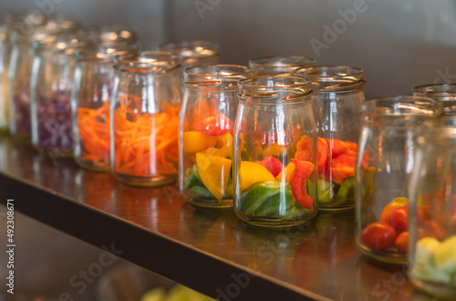Healthy fresh snacks from nature such as small pieces of Bell Pepper, Tomatoes, Carrots, Lettuce in small cleared-glass containers on stainless stell shelf. Perspective view