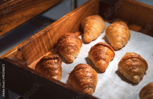 Row of brown crispy croissants in wooden tray or box, croissants are on white paper, dim light