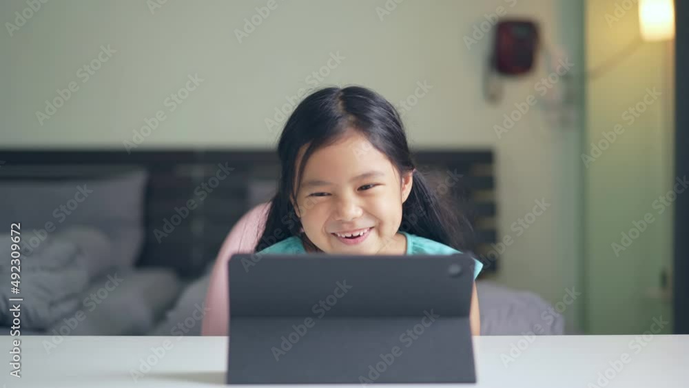 Asian child happy smile talking fun to teacher via video call learning on computer tablet or kid girl student enjoy laughing and studying online class or person learn from home school in bedroom Asian child happy smile talking fun to teacher via video call learning on computer tablet or kid girl student enjoy laughing and studying online class or person learn from home school in bedroom
