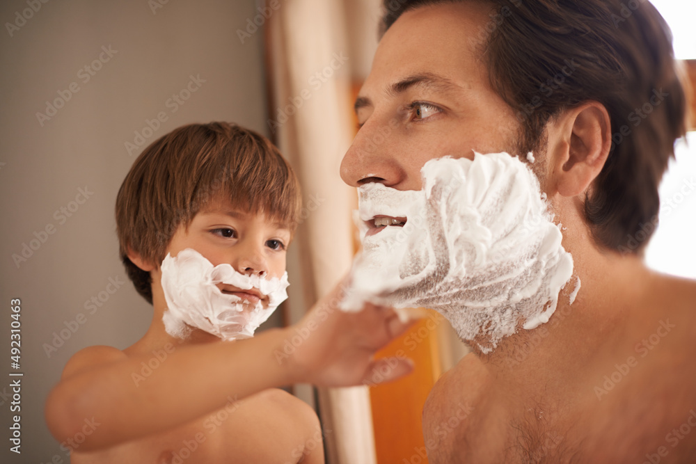 Hes got to learn some time. Shot of a little boy helping his father to shave.