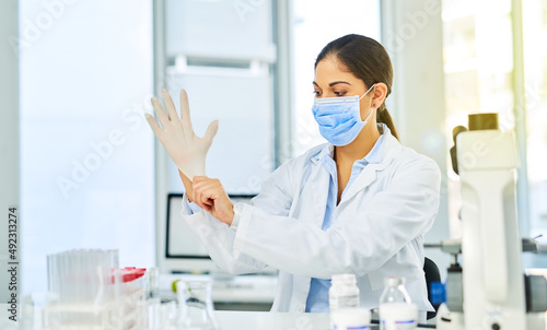 Ready to delve into some scientific research. Shot of a young scientist putting on protective gloves in a lab.
