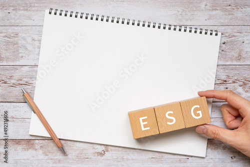 ESG投資のイメージ｜「ESG」と書かれた積み木とノートとペンと人の手