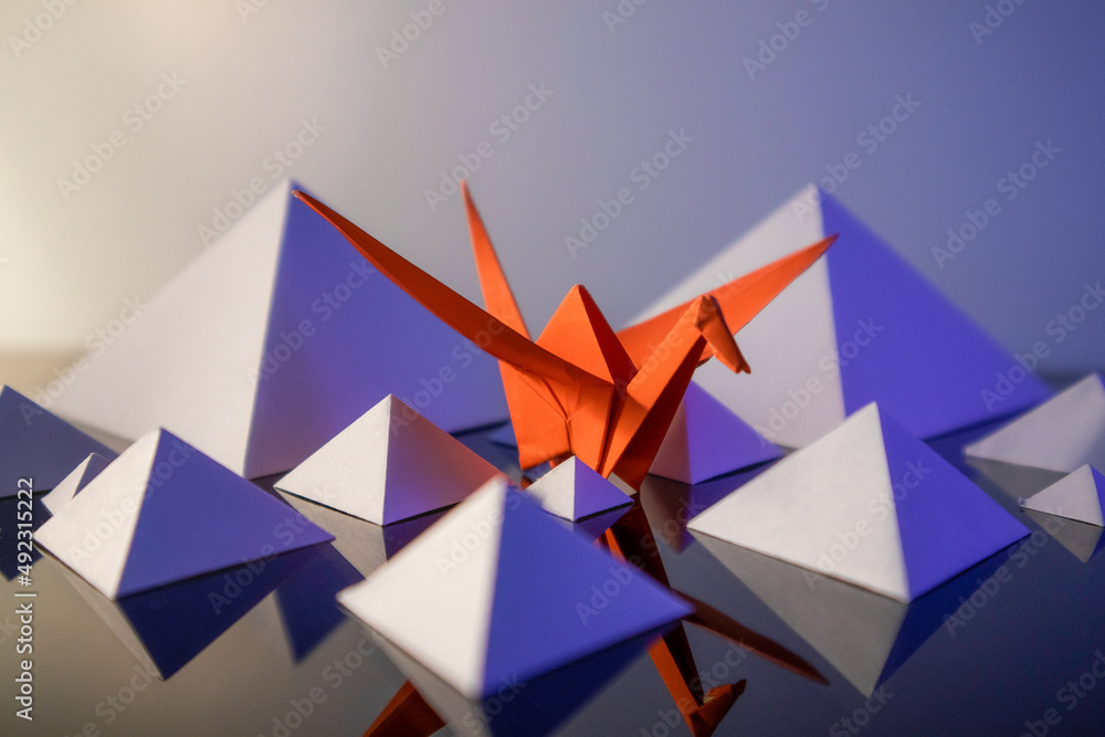 Fototapeta premium Orange origami swan in white paper pyramids 
