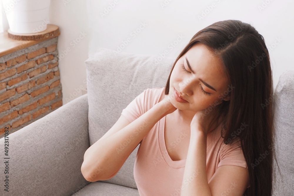 Young Asian woman touching her neck having neck pain at home Muscles tense up due to no stretching and relaxation Medical and healthcare concept Young Asian woman touching her neck having neck pain at home Muscles tense up due to no stretching and relaxation Medical and healthcare concept