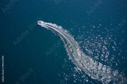 Modern white boat in a circular motion making a trail on the water. One boat on blue water drone view. Top view. Boat in turn fast moving aerial view. © Berg