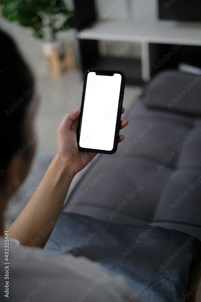 asia women holding smart phone with mockup white blank display, empty screen for app ads sitting on couch at home. Mobile applications technology concept, over shoulder close up view. asia women holding smart phone with mockup white blank display, empty screen for app ads sitting on couch at home. Mobile applications technology concept, over shoulder close up view.