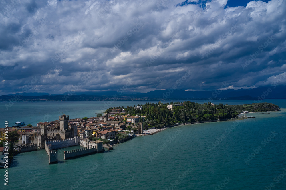 Rocca Scaligera Castle in Sirmione. Cumulus clouds over the island of Sirmione. Aerial view on Sirmione sul Garda. Italy, Lombardy.  Panoramic view at high altitude. Aerial photography with drone.