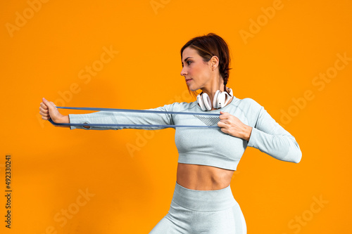 Atractiva mujer deportista haciendo ejercicios físicos con una banda elástica sobre un fondo de color naranja