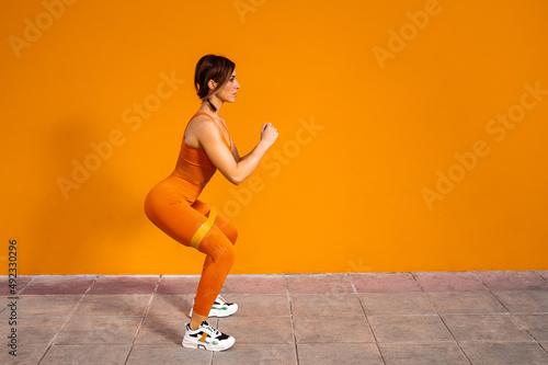 Atractiva mujer deportista haciendo ejercicios físicos con una banda elástica sobre un fondo de color naranja © Sergio Mena
