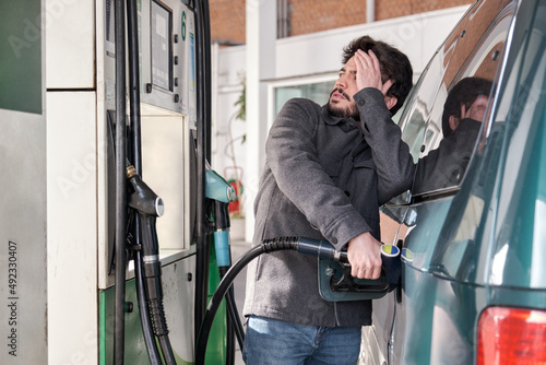 Картината върху платно Young man refueling his vehicle while looking worried at the high gas prices at a gas station