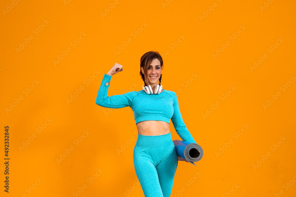 Alegre mujer deportista con unos auriculares haciendo ejercicios físicos sobre un fondo de color naranja Alegre mujer deportista con unos auriculares haciendo ejercicios físicos sobre un fondo de color naranja