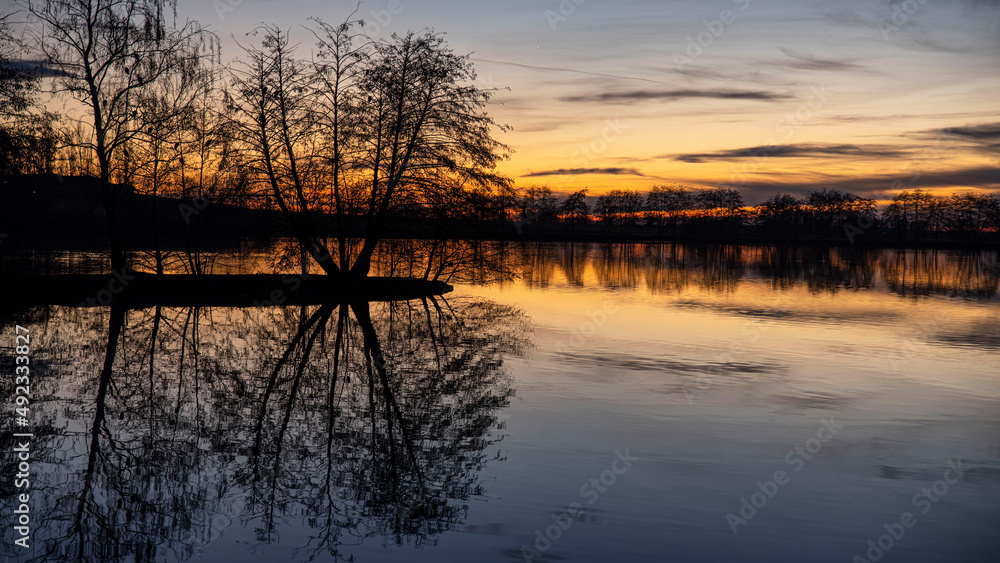 Sunset on a lake in Burgundy in France, with the black silhouettes of trees in winter Sunset on a lake in Burgundy in France, with the black silhouettes of trees in winter