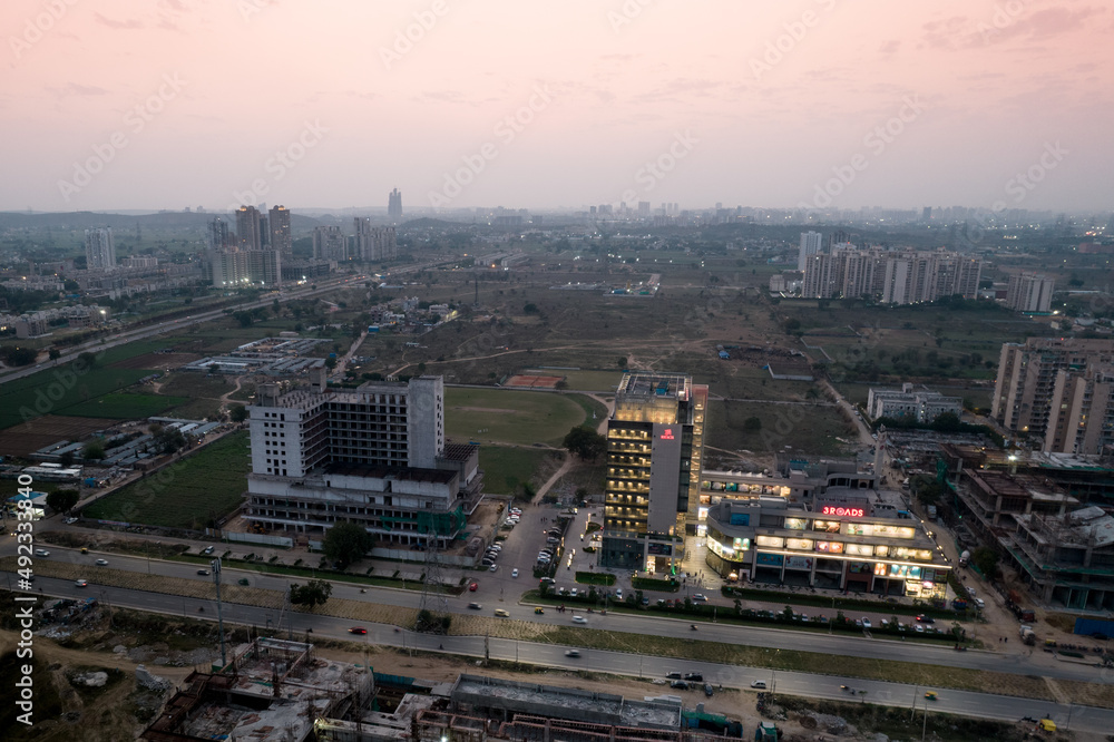 aerial dusk shot showing the 3 road shopping mall lit up with the under construction buildings around it unlit as the sun sets