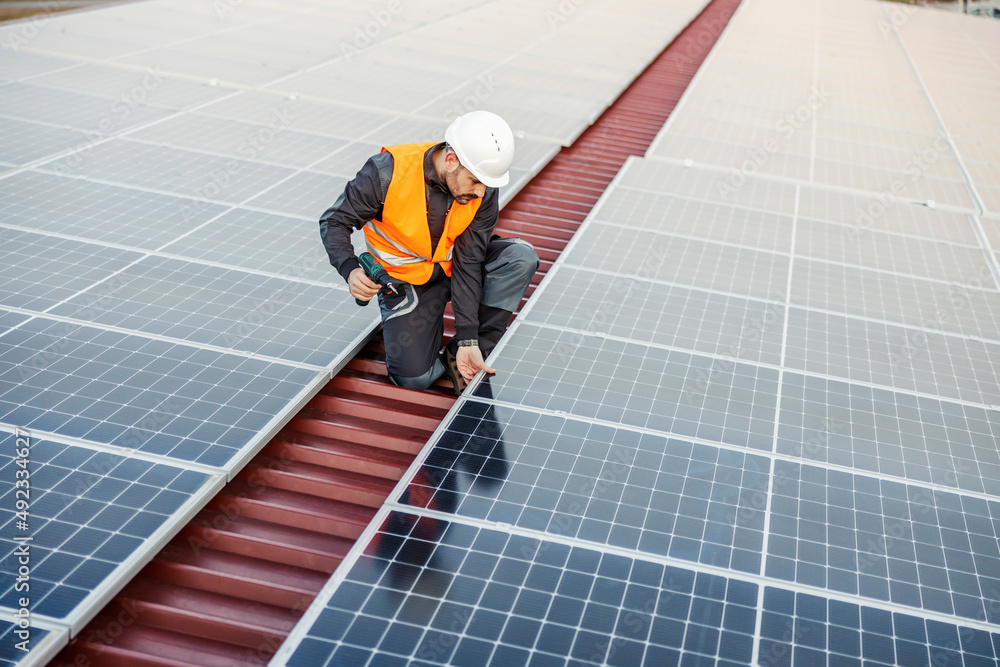 A worker installing solar panels on the roof. A worker installing solar panels on the roof.